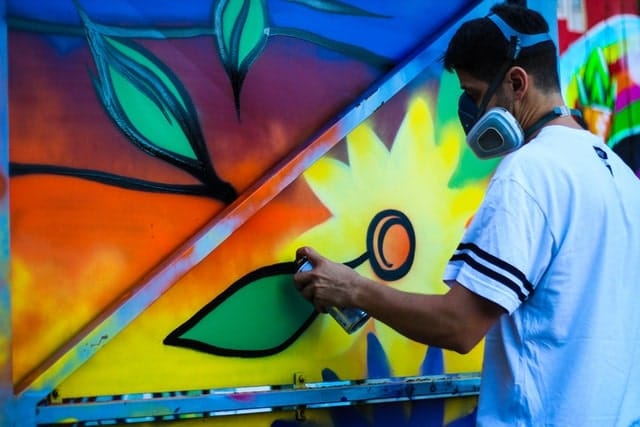 man wearing a respirator mask whilst spray painting a mural