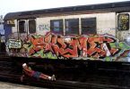 graffiti artist skeme laying in front of a painted train tagged with skeme