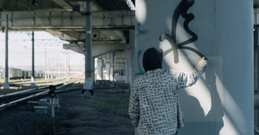 graffiti artist wearing hoodie tagging underneath an underpass